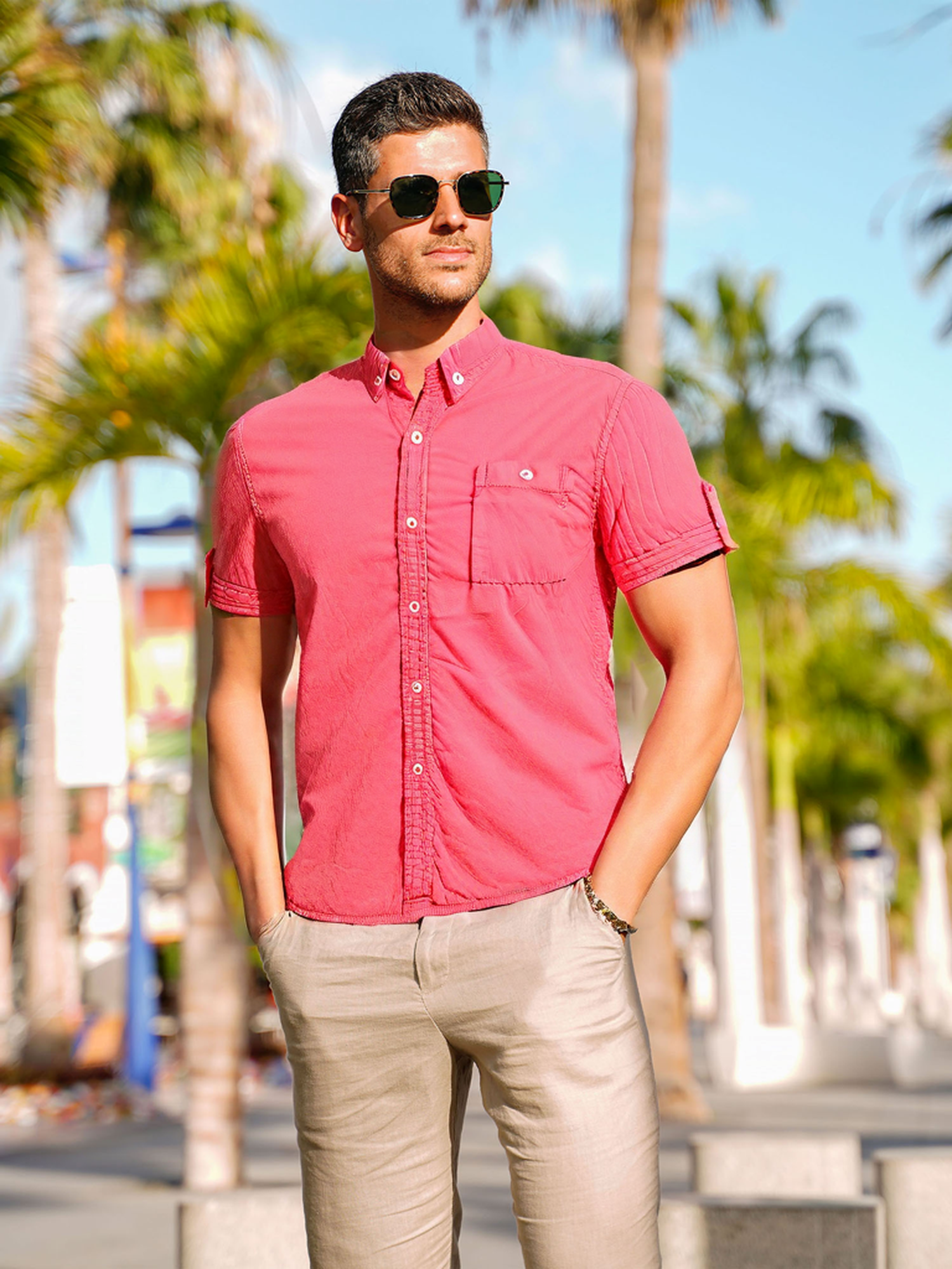 Un méchant portant des lunettes de soleil, regardant vers la gauche, portant une chemise boutonnée rose-rouge.