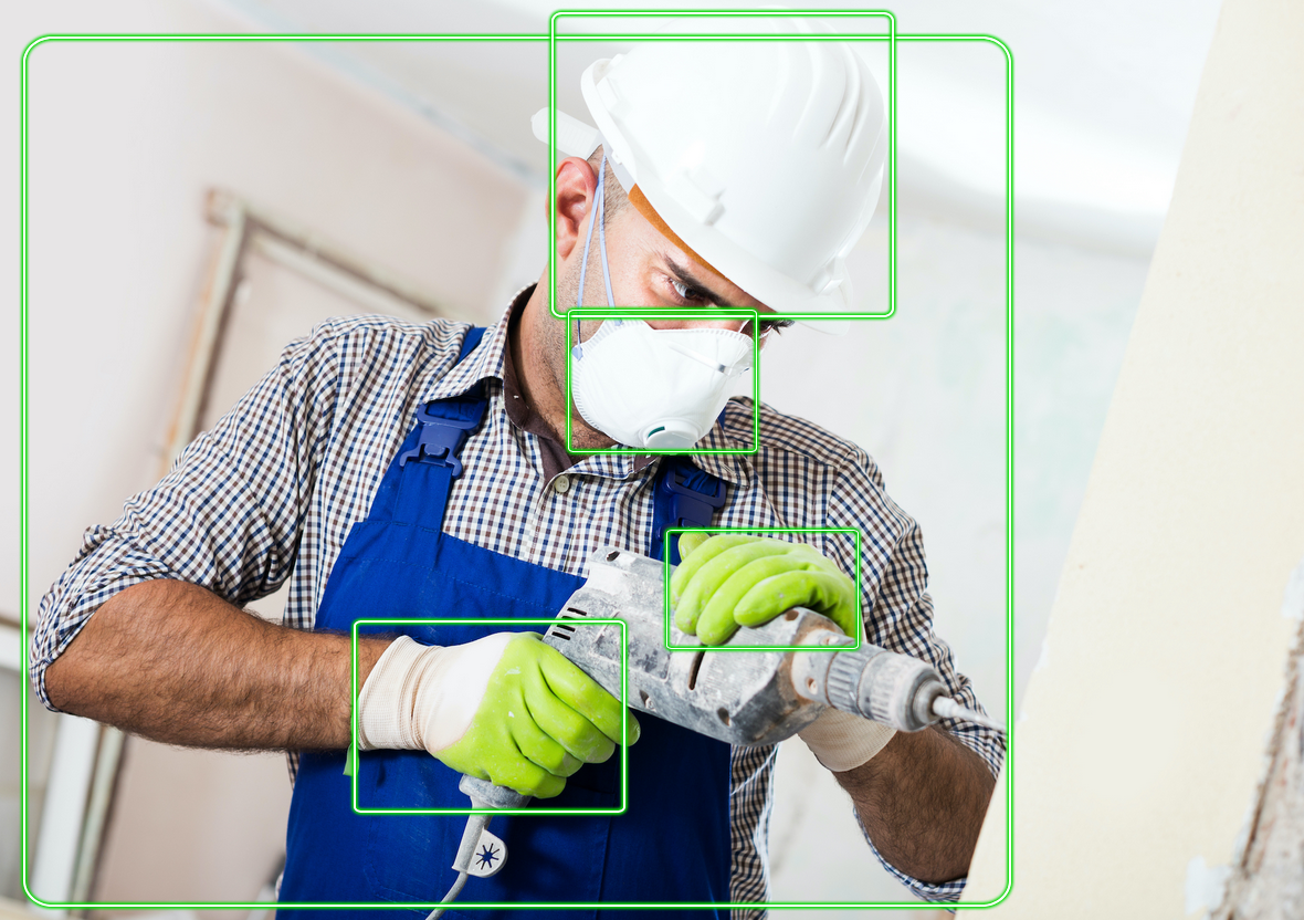 Pekerja yang memakai APD termasuk hardhat, kacamata pengaman, masker pelindung, dan sarung tangan, mengoperasikan perkakas listrik. Membatasi kotak di sekitar item.