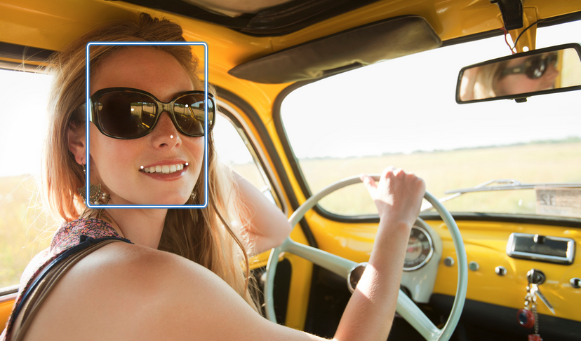 Smiling woman wearing sunglasses and driving a vintage yellow car on an open road.